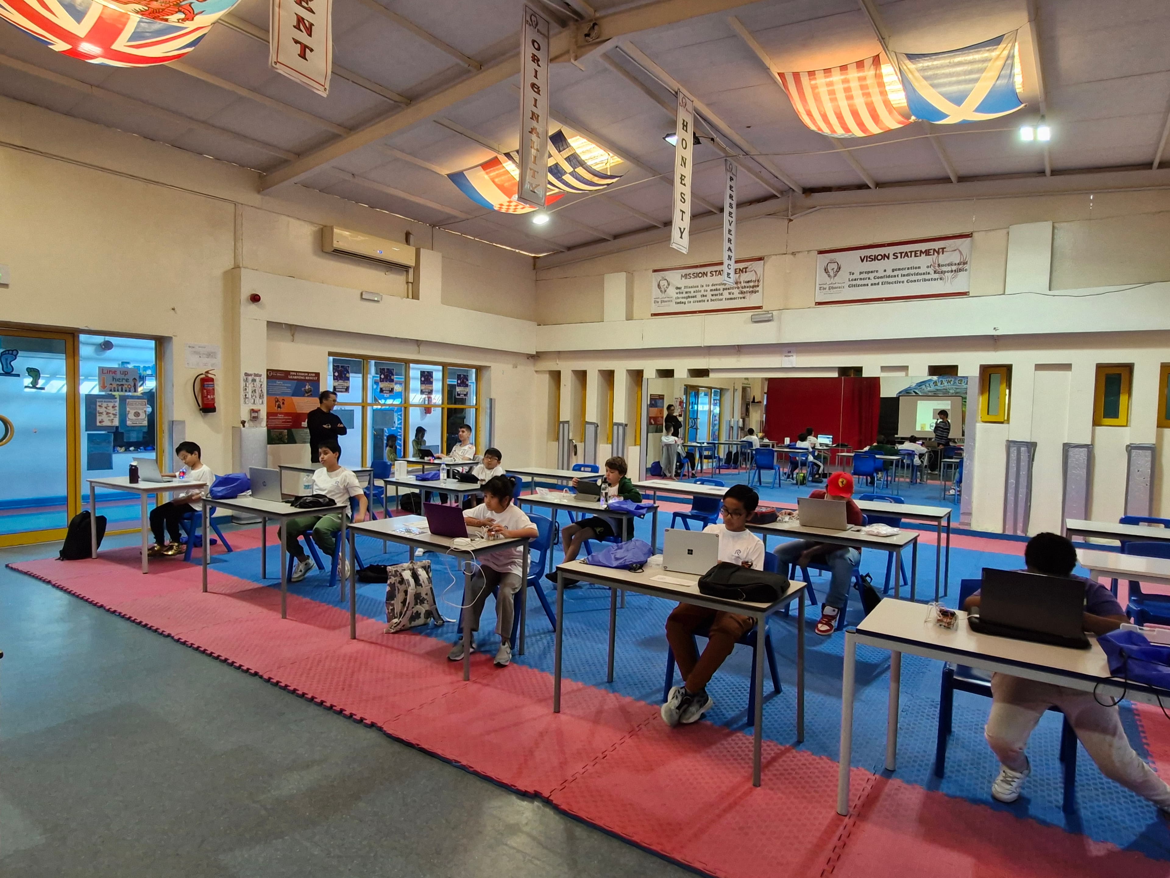 Wide classroom view of students programming robots on laptops